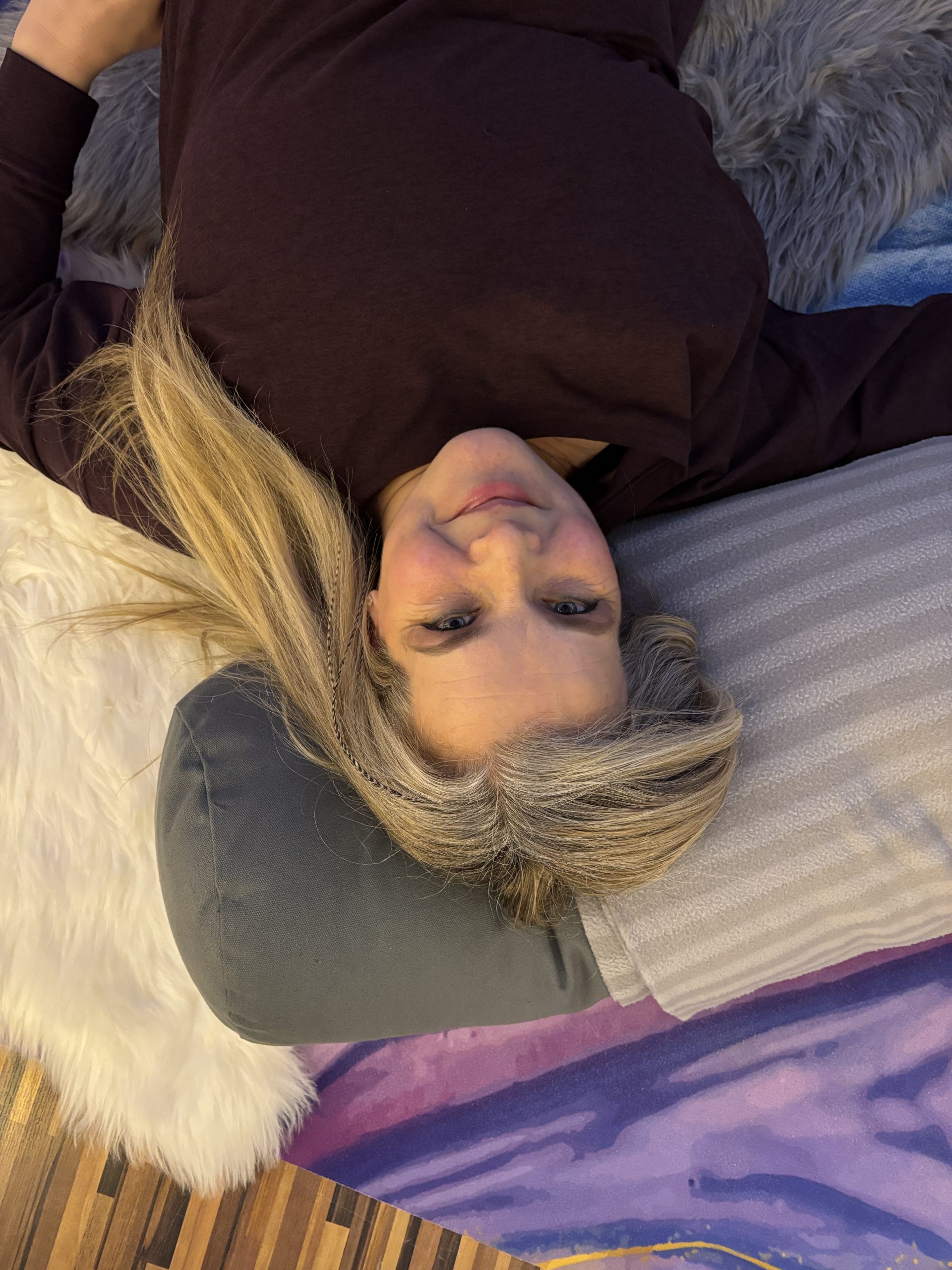 Nadine Hill, yoga teacher, laid on yoga mat and pillows cushions, cosy, in her studio.